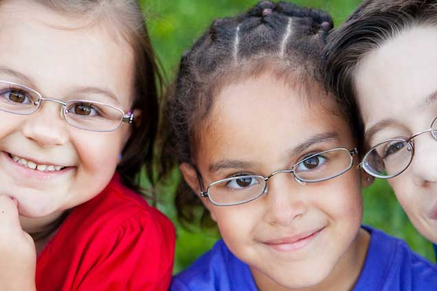 Smiling children wearing eyeglasses outdoors.